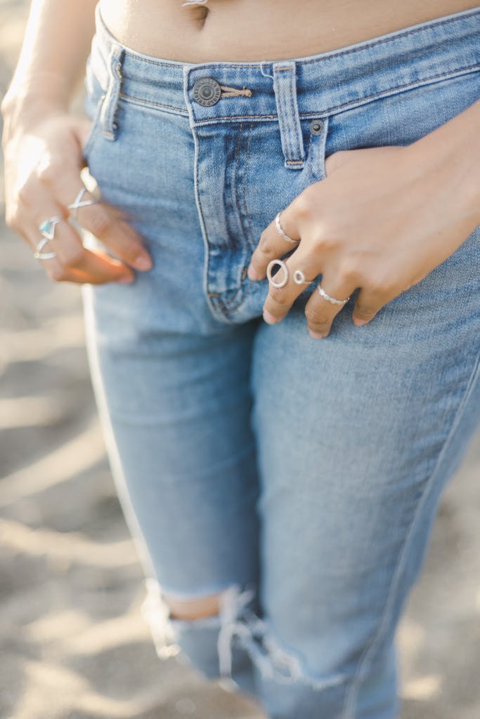 Crop anonymous female in trendy denim clothes standing with hands in pockets with collection of silver rings on fingers